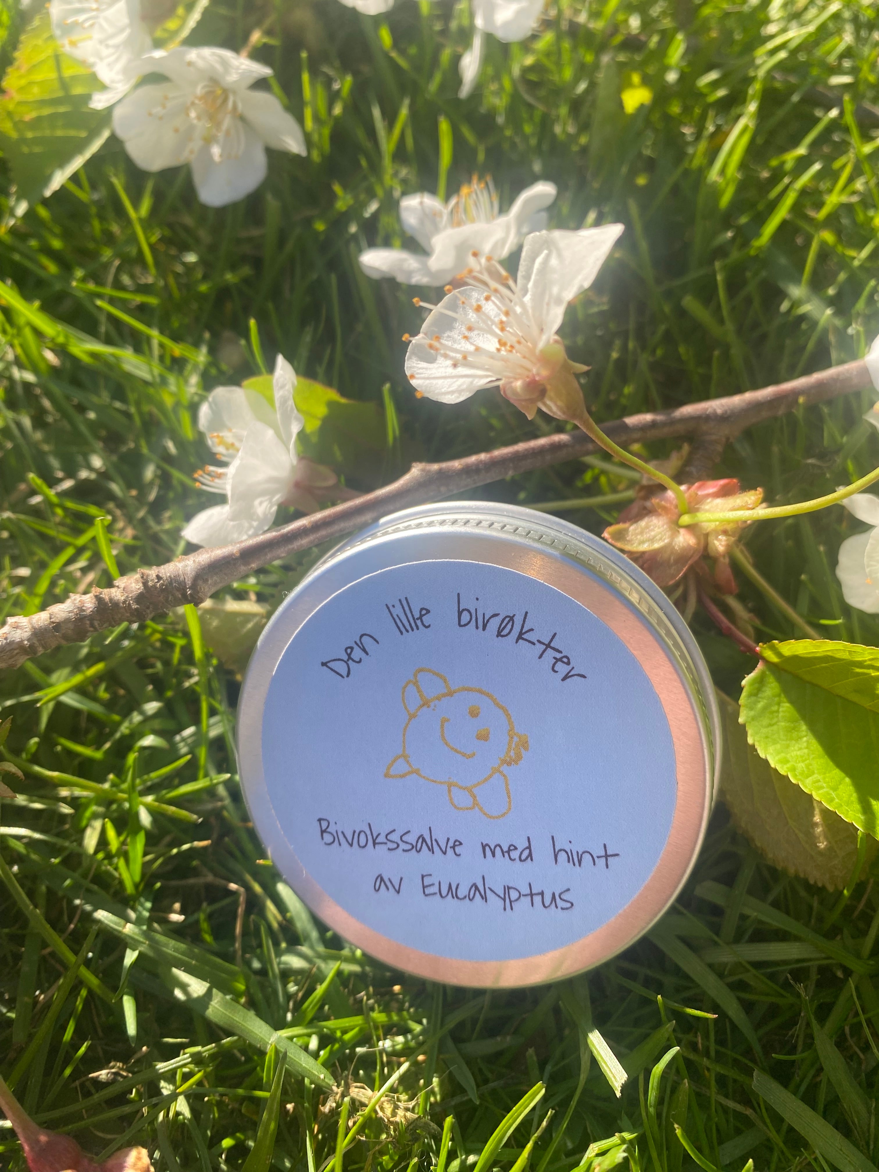 Bivokssalve med blå etikett. Ligger i gress med epleblomster rundt